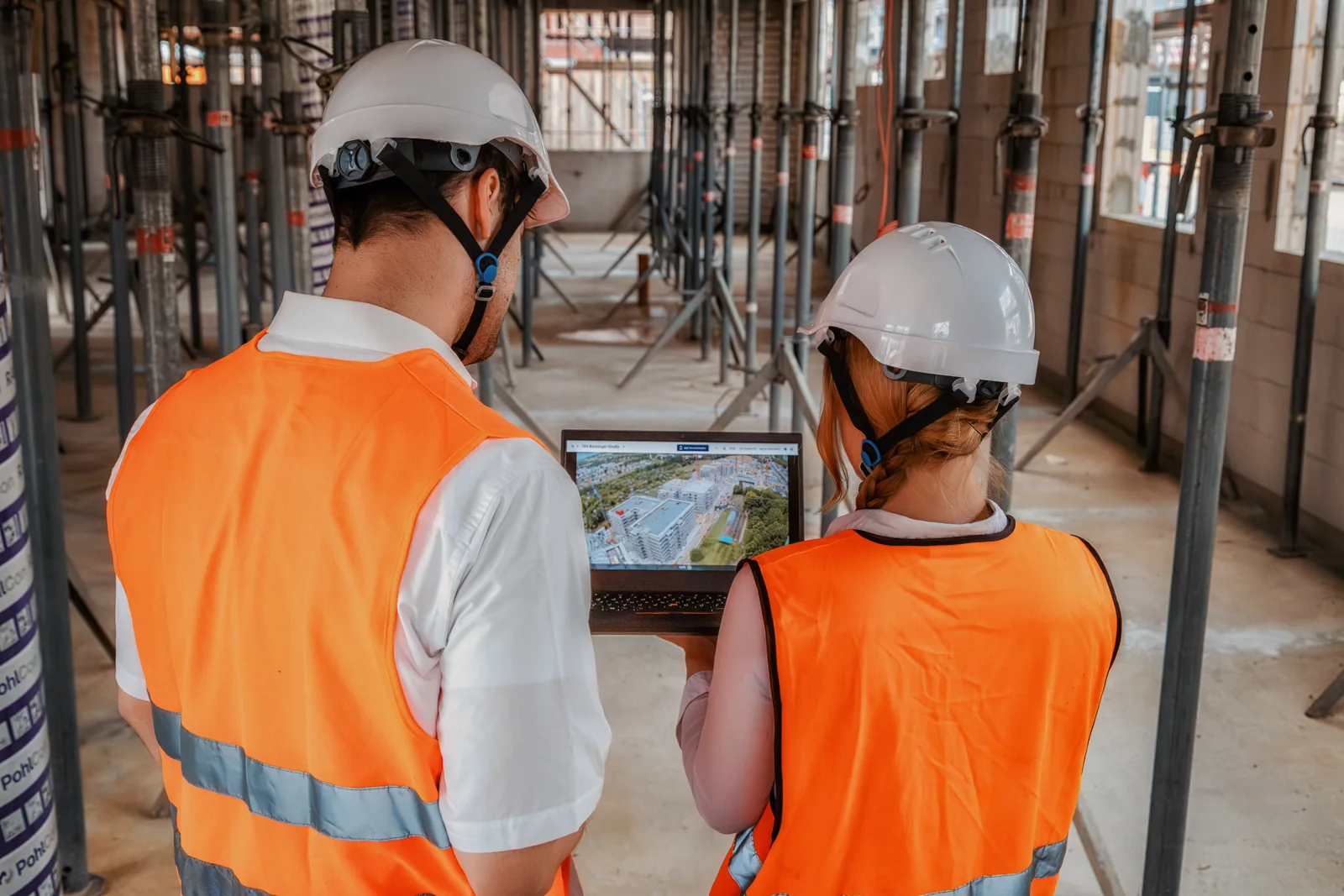 Two people checking the BauTV+ portal on a laptop in the shell construction